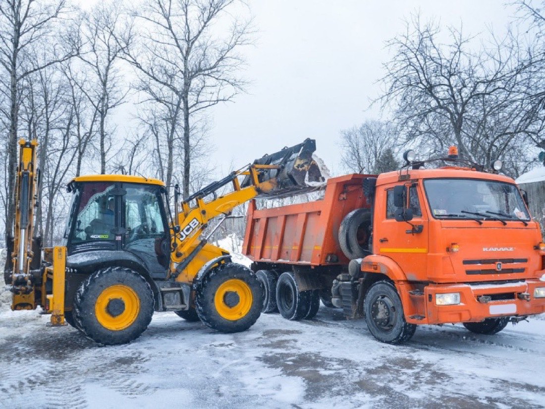 Экскаватор-погрузчик JCB грузит снег в самосвал КАМАЗ